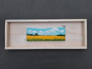 Schilderijtje met koolzaad en daarachter het dorp Stedum